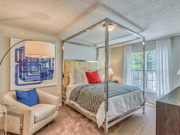 A bedroom with a four poster bed and a blue chair.