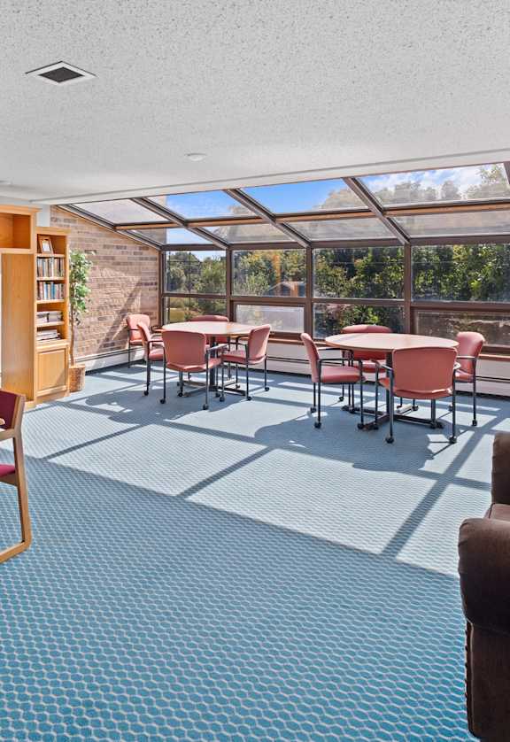 A sunny day in a room with a table, chairs and a bookshelf.