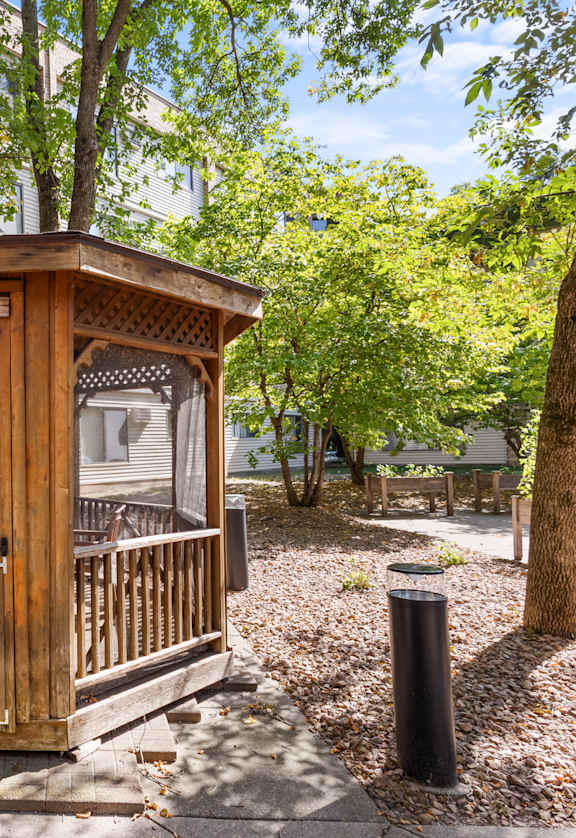 A wooden gazebo is situated in a grassy area in front of a building.