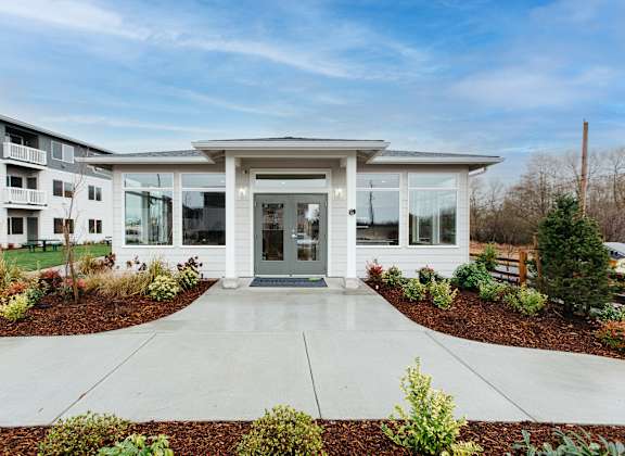A modern building with a white entrance and a landscaped garden in front.