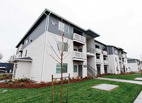an apartment building with white siding and green grass