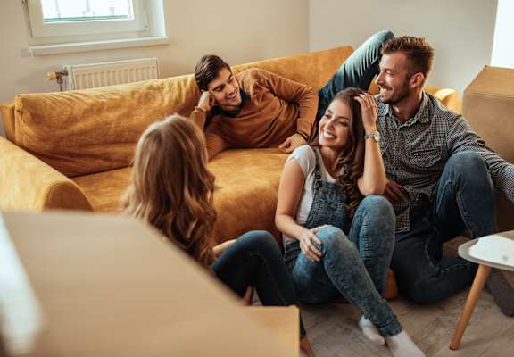 Four people sitting on a yellow couch in a living room.