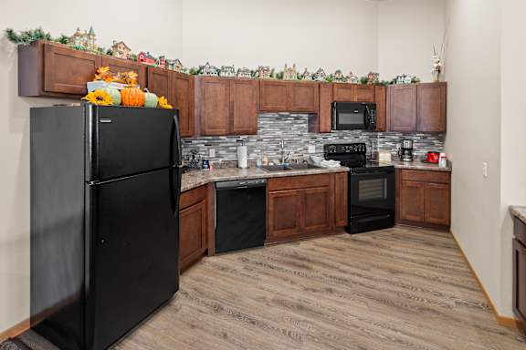 A black fridge stands in a kitchen with wooden cabinets and a stone backsplash.