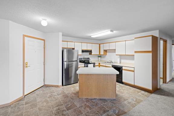 A kitchen with a refrigerator, sink, and cabinets.