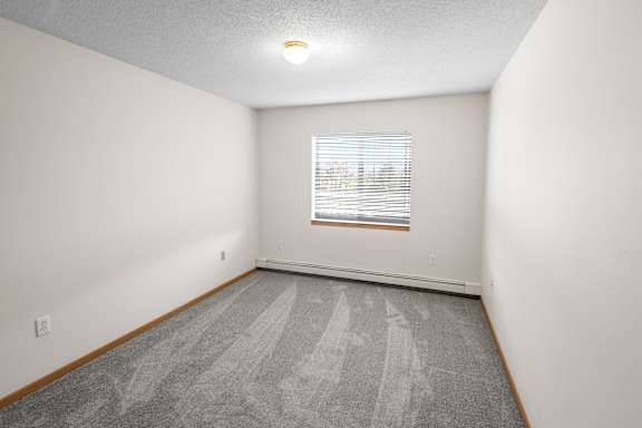 A room with a carpeted floor and a window with blinds.