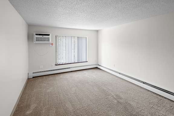 A room with a carpeted floor and a window with blinds.
