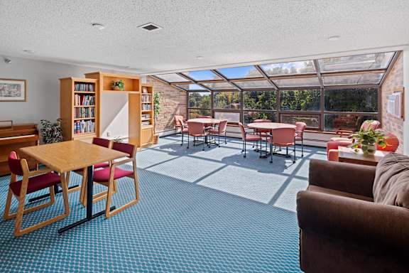 A sunny day in a room with a table, chairs and a bookshelf.