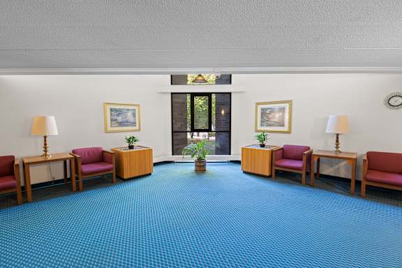 A waiting room with red chairs and a blue carpet.