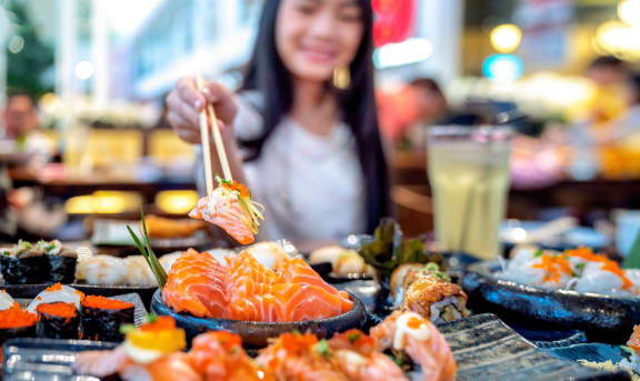 a woman eating sushi at a restaurant with chopsticks