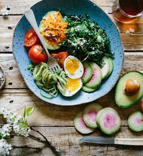 A blue bowl filled with a salad and various vegetables on a wooden table.