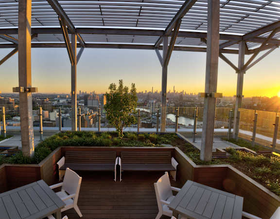 a rooftop terrace with a bench and tables and a view of the city skyline
