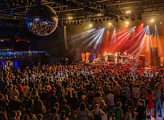 A large crowd of people are gathered in a dark room watching a performance on a stage.