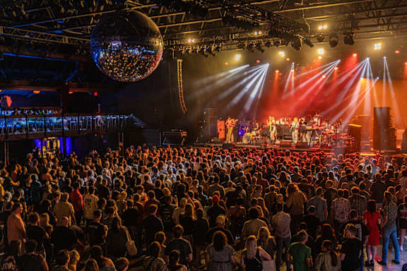 A large crowd of people are gathered in a dark room watching a performance on a stage.