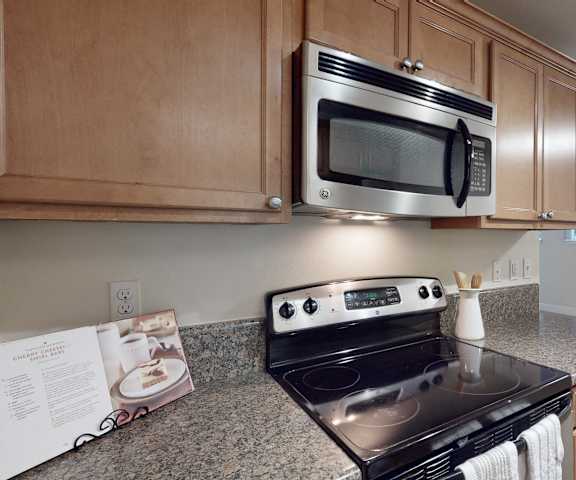 A cozy kitchen with black appliances, spacious marble countertops, and large wooden cabinets with decorations at Regency Woods Apartment Homes. 