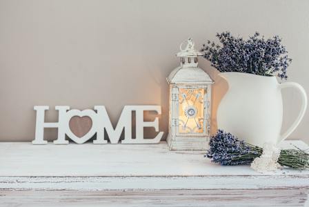 A white ceramic mug with a bouquet of lavender flowers and a white lantern with a lit candle inside, placed on a white wooden surface.