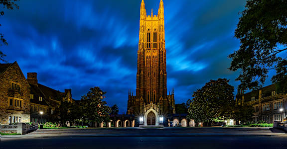 A tall tower stands in the center of a courtyard surrounded by buildings.