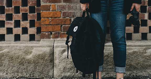 A person is standing with a black backpack on their back.