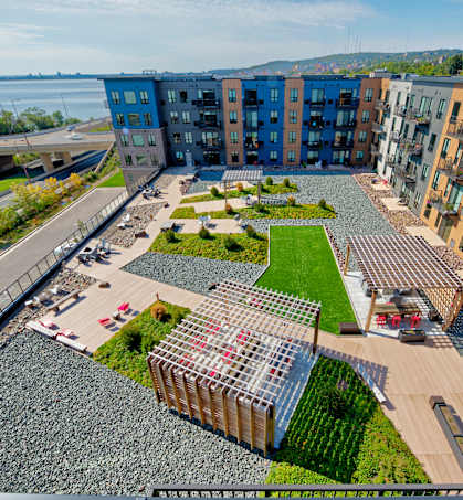 A modern apartment complex with a green courtyard and a body of water in the background.