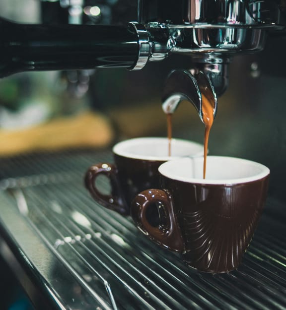 two cups of coffee being poured into a espresso machine