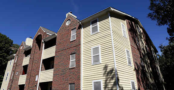 A tall apartment building with a red brick base and beige siding.