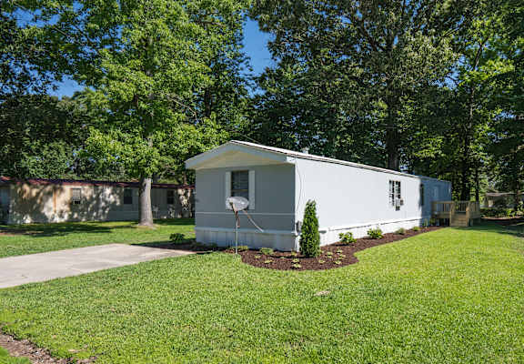 a small blue and white mobile home in a yard with grass and trees