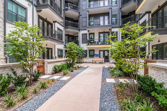 A courtyard with a concrete pathway and a bench surrounded by plants and trees.