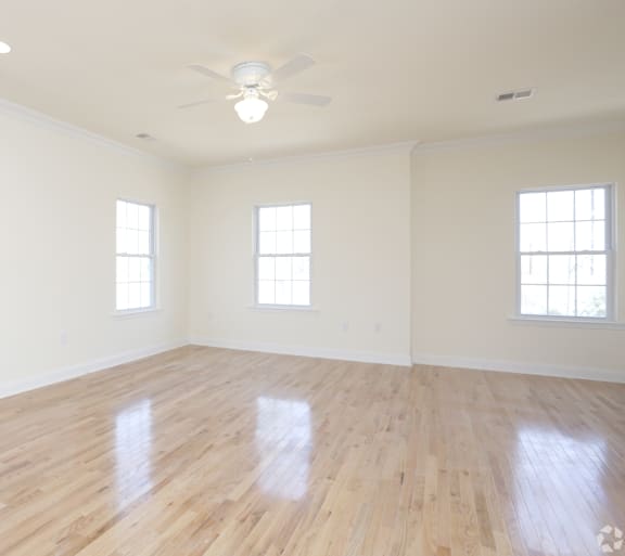 an empty room with a ceiling fan and three windows
