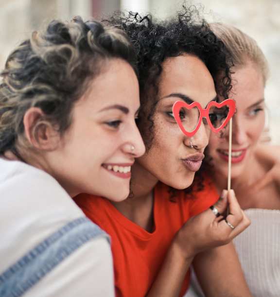Two women are sitting close together, one is holding a red heart-shaped lollipop.