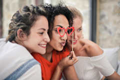 Two women are sitting close together, one is holding a red heart-shaped lollipop.