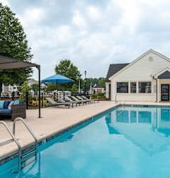 A pool with a blue umbrella and a white building in the background.