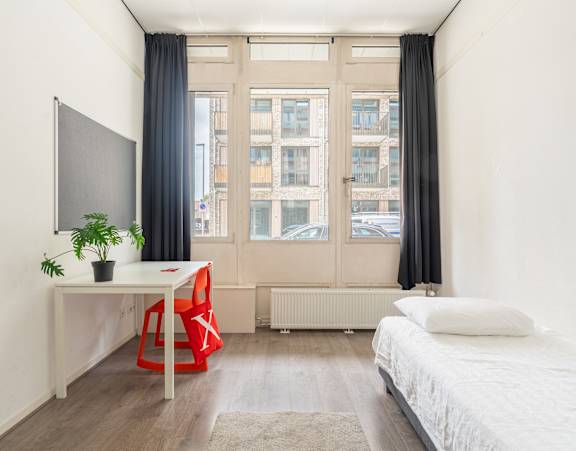 A room with a bed, desk, chair, and window.