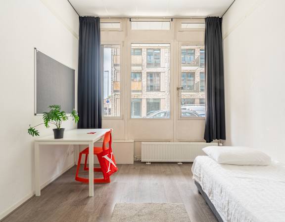 A room with a bed, desk, chair, and window.
