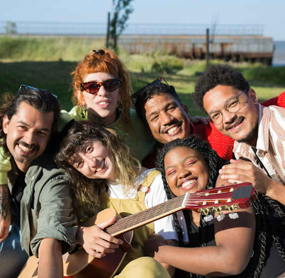 A group of friends are sitting on the grass with a guitar.