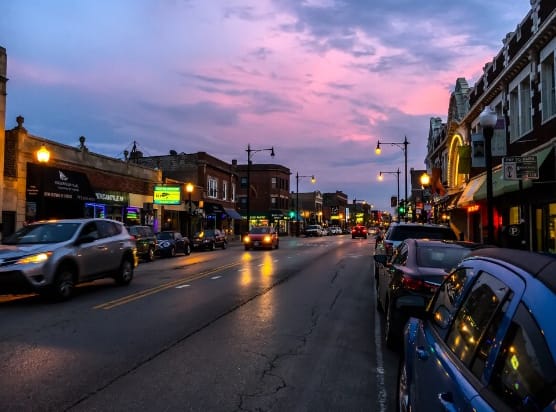 a city street at sunset with cars parked on the side of the road