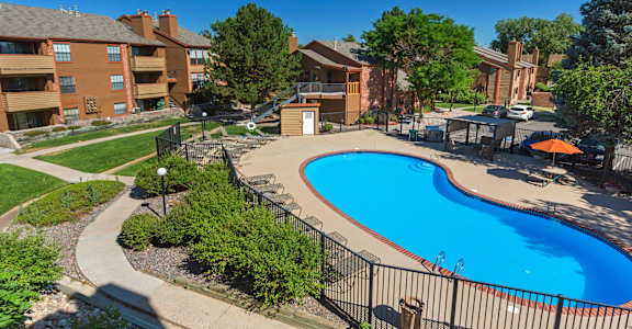 A swimming pool surrounded by a black fence and a grassy area with trees.