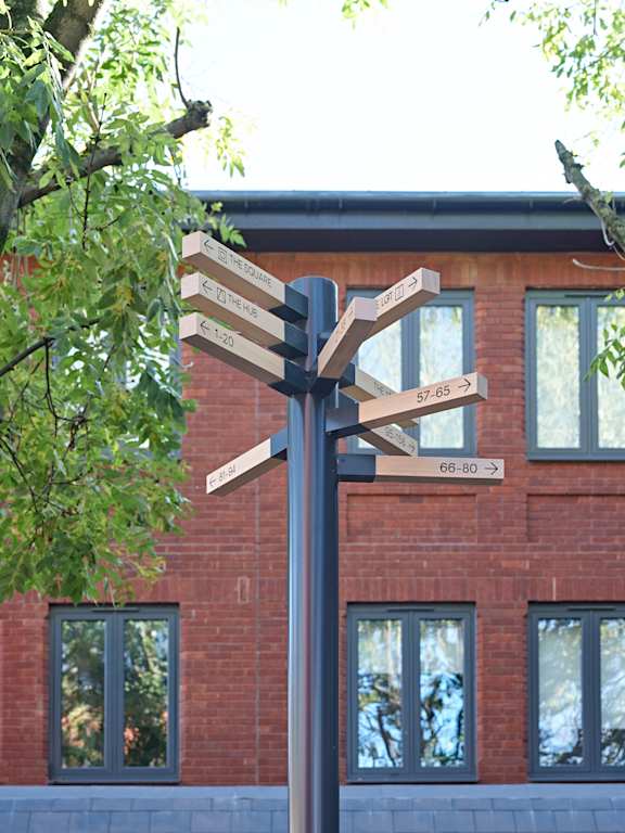 A signpost with multiple directions and distances in front of a brick building.