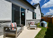 Thumbnail 3 of 4 - A patio with a grey couch and a striped pillow is in front of a house.