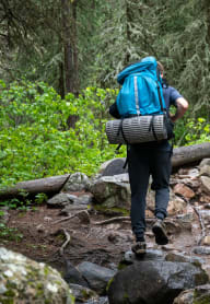 A man with a blue backpack is crossing a stream in the forest. at Autumn Village, Washington, 98354