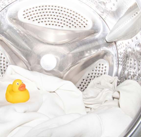A yellow rubber duck sits on a white towel inside a washing machine.