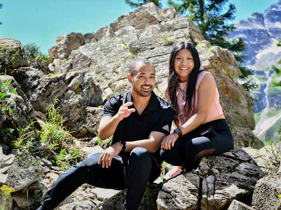 A man and a woman are sitting on rocks in a natural setting.