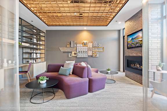 A living room with a purple couch, a fireplace, and a painting on the wall.