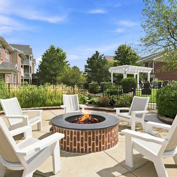 A fire pit surrounded by white chairs in a backyard.