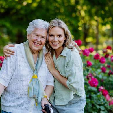 An elderly woman and a younger woman are standing in a rose garden.