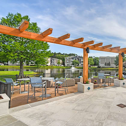 a patio with tables and chairs and a wooden pergola overlooking a lake at Reserve at Gulf Hills Apartment Homes in Ocean Springs, MS 39564