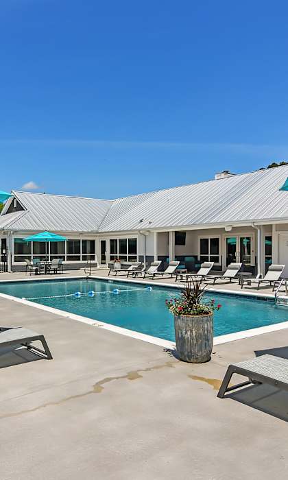 A large swimming pool area with sun loungers and umbrellas. at The Woodlands Apartment Homes, Meridian, MS, 39301