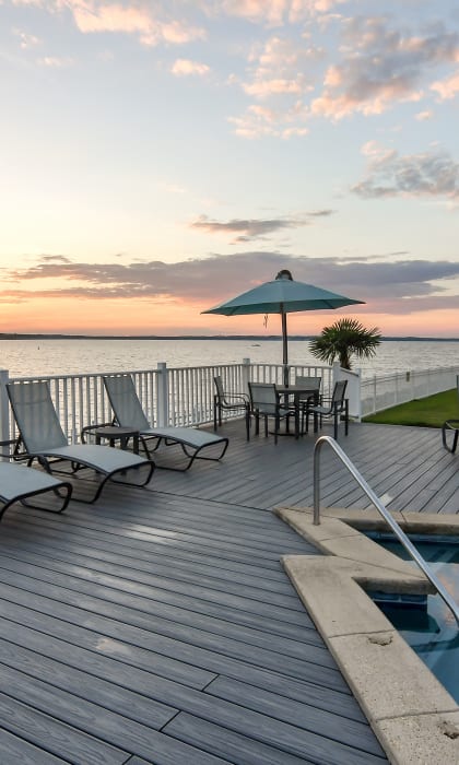 a deck with chairs and a pool overlooking the water at sunset at Lakeshore Pointe Apartment Homes, Brandon, 39047
