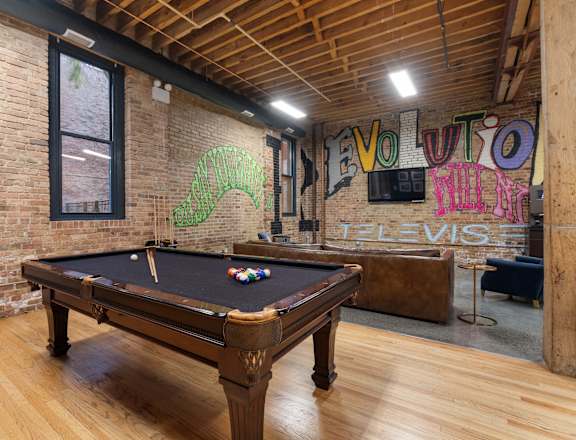 A pool table in a room with a brick wall and wooden floors.