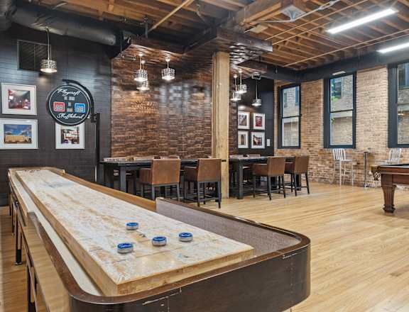 A shuffleboard table is in the middle of a room with brick walls.