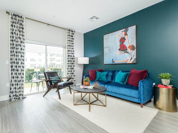 A living room with a blue couch and a painting of a woman on the wall.