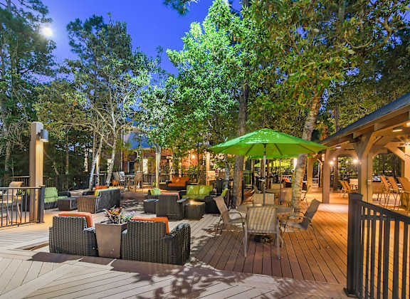 A deck with a green umbrella and chairs is surrounded by trees.
